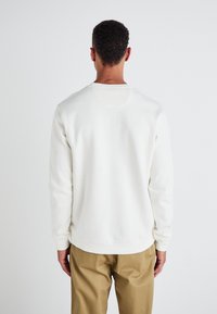 Sweatshirt en coton blanc à manches longues, col rond et poignets côtelés. Texture lisse, légère taper à la taille et sans motifs visibles.
