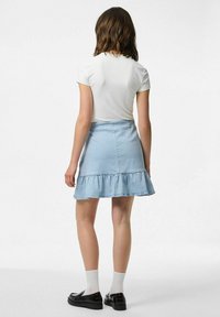 Šviesiai mėlyna džinsinė sijonas su volaniniu apvadu, derinama su prigludusia balta palaidine. Aprangą užbaigia juodi batai ir baltos kojinės.