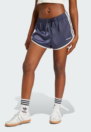 Pantaloni sportivi blu navy con bordi bianchi, vita elastica e cordino. Abbinati a scarpe bianche e calze a righe.