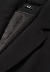 Blazer noir avec doublure intérieure à motifs et étiquette de marque C&A visible dans la zone du col.