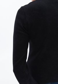 Schwarzes Langarmoberteil aus weichem Stoff, mit tailliertem Design und rundem Ausschnitt, mit sichtbaren Nähten entlang der Nähte.