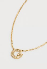 Gouden ketting met een ronde "G" hanger versierd met heldere rhinestones, geplaatst op een delicate ketting met vergrendelbare schakels.