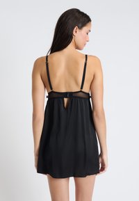 Czarna satynowa nocna sukienka z regulowanymi ramiączkami. Posiada przeźroczysty siateczkowy tył oraz małe wycięcie w kształcie klucza. Miękka, lekko opływająca tkanina, długość powyżej kolan.