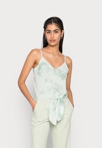 Camisola de alças finas em tie-dye verde claro com decote em V, combinada com calças altas verde claro e tecido amarrado na cintura.