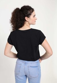 Černý top s krátkým rukávem a kulatým výstřihem, nošený s světle modrými džíny. Materiál vypadá jemně, má volný střih a jednoduchý design.