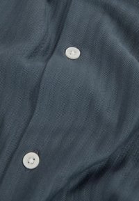 Tela texturizada de un gris oscuro con suaves ondas, que presenta botones blancos. La vista de cerca enfatiza la superficie suave del material y su artesanía.