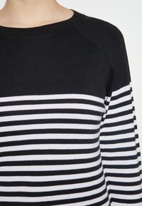 Gestreifter Pullover in Schwarz-Weiß, mit Rundhalsausschnitt und gerippter Textur, der abwechselnd kräftige horizontale Streifen zeigt.