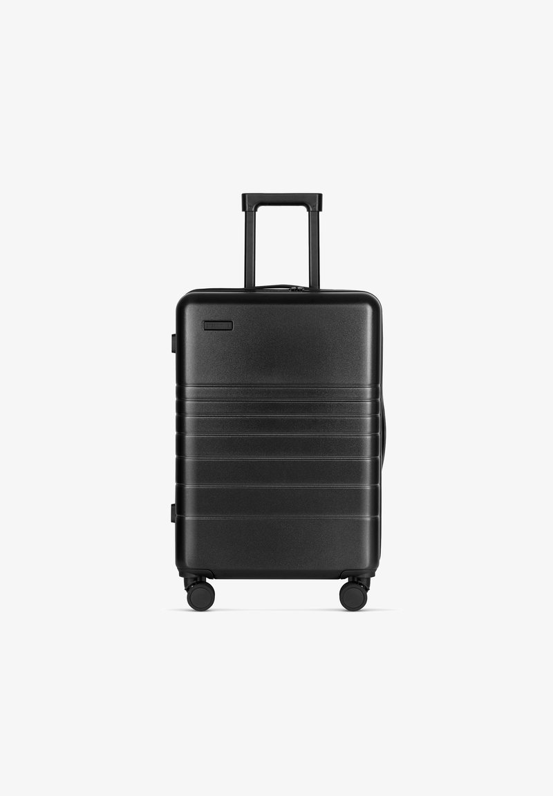 Schwarzer Hartschalenkoffer mit glatter Oberfläche, horizontalen Rillen, ausziehbarem Griff und vier Rädern für einfache Mobilität.