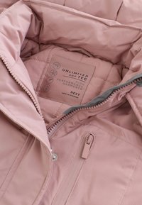 Intérieur de veste isolante rose avec texture matelassée, poche à fermeture éclair et étiquette d'entretien mettant en avant la performance "UNLIMITED TEC".