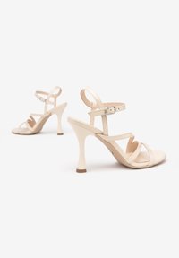 Beige strappy high heelsandalen met een gladde leren afwerking, voorzien van drie gekruiste banden en een smalle enkelband op een slanke hak.
