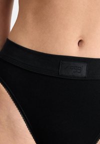 Zwarte katoenen slips met een brede tailleband en een textuur logo patch. Beschikt over een gegolfde rand langs de beenopeningen voor extra detail.