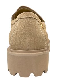 Beige suède schoen met een platte, gestructureerde zool, ronde neus en verhoogde hak. Kenmerkt zich door stiksels en een kleine metalen accent aan de zijkant.