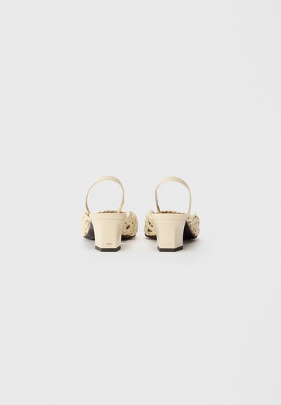 Sandalias de tacón beige con un patrón tejido, punta cuadrada y tacón sólido. Cuenta con una fina correa en el tobillo y una parte superior texturizada.