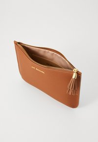 Clutch in finta pelle marrone con zip dorata, interno foderato e accentuazione con nappina decorativa. Presenta il logo del brand in rilievo sulla parte anteriore.