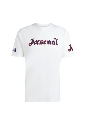T-shirt en coton blanc avec un grand texte "Arsenal" en rouge et bleu marine sur le devant. Manches courtes avec des rayures bleues marines Adidas sur la manche gauche.