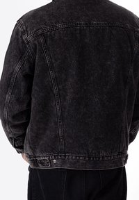 Svart jeansjacka med en avslappnad passform, synliga sömmar och en något nöttyra textur. Har en klassisk krage och knäppta ärmslut.