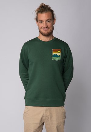 Green sweatshirt made of cotton with a crew neck, featuring a colorful graphic patch with mountains, sun, and "GOOD VIBE" text on the chest.