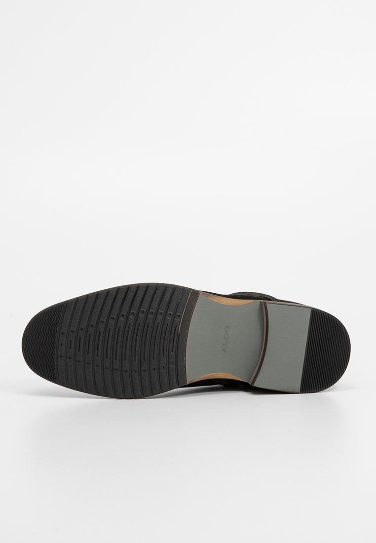 Schwarze Gummisohle mit einem strukturierten Profil für besseren Halt, einem hellgrauen Bereich in der Mitte und einem glatten braunen Akzent.