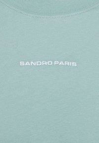 Lys grøn bomulds t-shirt med rund hals og centralt hvidt broderet tekst "SANDRO PARIS." Glat tekstur med minimalistisk design.