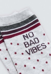 Calcetines en gris claro con puños a rayas en color burdeos y gris oscuro, que presentan el texto "NO BAD VIBES" y pequeños lunares burdeos.