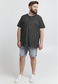 Cămașă henley gri închis, cu mânecă scurtă și patru nasturi, asociată cu pantaloni scurți din denim deschis și sneakerși albi. Design simplu, casual.