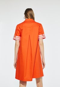 Vestito corto arancione con colletto e piega sul retro, caratterizzato da polsini a righe bianche e rosa, realizzato in un tessuto liscio.