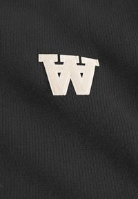 Black knit fabric with a prominent embroidered beige letter "W" in a stylized font. The texture is smooth with a slight ribbed pattern.