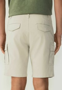 Shorts cargo beige avec une coupe structurée, dotés de deux poches arrière et de poches latérales, fabriqués en tissu léger et lisse.