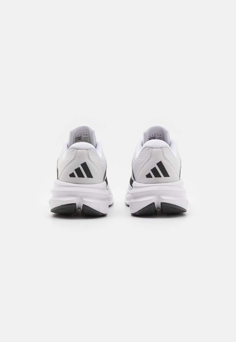Baskets de sport blanches au design épuré. Présentent des accents noirs et un branding à trois bandes. Matériau texturé avec des semelles rembourrées.