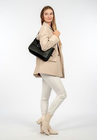 Svart läderhandväska med texturerad yta, silverfärgad hårdvara och en axelrem. Buren med en beige blazer och vita byxor.