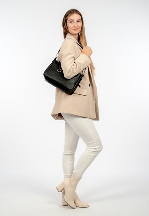 Schwarze Lederhandtasche mit strukturiertem Finish, silberner Hardware und Schultergurt. Getragen mit einem beigen Blazer und weißen Hosen.