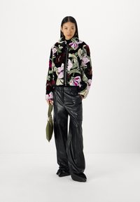 Fuzzy black jacket with large floral embroidery in pink and green tones, paired with high-waisted black leather trousers and a green handbag.