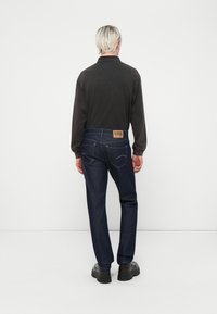 Mørk langermet polo-skjorte kombinert med mørke denim jeans; jeansene har en brun skinnlapp i midjen og tradisjonell baklomme-søm.