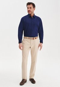 Granatowa koszula zapinana na guziki, beżowe chinosy, brązowy pasek i ciemne buty. Koszula ma klasyczny kołnierzyk i gładką fakturę materiału.
