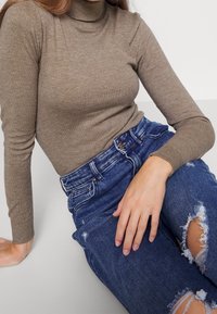 Ribattu turtleneck kastanjanvärinen toppi yhdistettynä kuluneisiin sinisiin farkkuihin, joissa on revityksiä, klassinen vyötärö ja rento istuvuus.