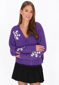 Cardigan fuzzy purpuriu cu decolteu în V și mâneci lungi, având modele de fulgi de zăpadă albi pe mâneci și un închizător cu un singur buton.