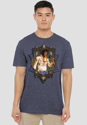 Young man wearing a navy blue T-shirt featuring Elvis Presley in a white suit with "Aloha from Hawaii" text and floral design.