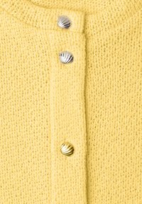 Tissu tricoté jaune avec trois boutons en forme de coquille en argent et or le long d'une couture verticale.