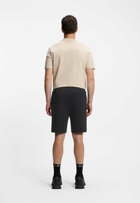 Camicia beige chiaro a maniche corte, abbinata a pantaloni neri. La camicia ha una texture liscia; i pantaloni sono lunghi fino al ginocchio con un design semplice.