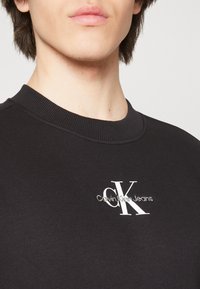 Black sweatshirt made of cotton with a ribbed neckline, featuring a white Calvin Klein Jeans logo and sleek, minimal design.