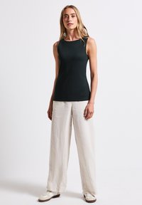 Musta ilmanhiha toppi, joka on valmistettu sileästä kankaasta, yhdistettynä kevyisiin, leveisiin pellavahousuihin. Mallilla valkoiset tennarit ja vähän asusteita.