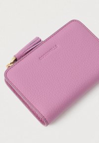 Kompaktiška tekstūruota rožinė odinė piniginė su siūtu kraštu, išlenktu prekės ženklu ir auksiniu užtrauktuku su atitinkamu odiniu kutu.