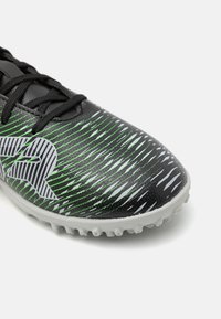 Schwarze Sportschuhe mit grünen und weißen grafischen Mustern, strukturiertem Obermaterial, schwarzen Schnürsenkeln und einer weißen Gummisohle mit kurzen Stollen.