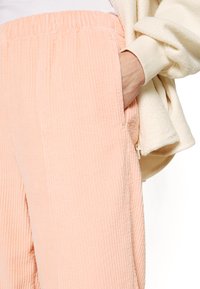 Brožové kordové kalhoty s elastickým pasem a boční kapsou, které jsou zkombinovány s krémovým fleecovým svetrem, zdůrazňující texturovanou látku.