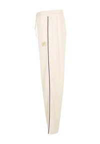 Kremowe spodnie dresowe z elastycznym pasem, fioletowym paskiem po boku, sznurkiem oraz małym haftowanym logo marki na lewym udzie.