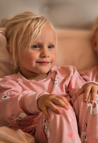 Pink cotton pajamas featuring playful animal patterns, with gathered sleeves and cuffs, worn by a child seated comfortably.