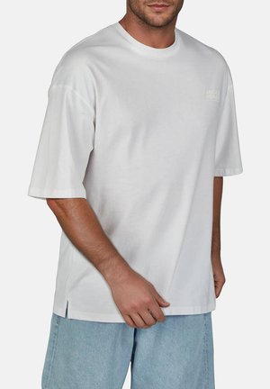 Witte katoenen t-shirt met korte mouwen en ronde hals, met een subtiele logo op de bovenste linkerkant en een rechte zoom met zijsplitten.