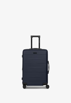 Maleta rígida azul marino con ranuras horizontales, asa retráctil negra, cuatro ruedas y asa lateral para llevar. Textura suave y diseño duradero.