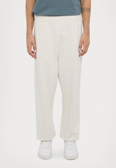 Cream-colored sweatpants with an elastic waistband, relaxed fit, and smooth texture, paired with white sneakers.