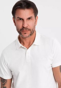 Vit polo t-shirt med texturerad tyg, tvåknappsknäppning och korta ärmar. Inkluderar en diskret logotyp på bröstet och en klassisk krage.